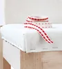 A close-up view of a white fabric seat cushion on a wooden chair, with a roll of red and white decorative ribbon on top. Produktbild-Vorschau