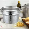 A stainless steel pasta pot with a steamer insert sits on a kitchen counter next to uncooked pasta, garlic, and a bottle of olive oil. Produktbild-Vorschau