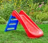 A red and blue plastic slide for children is set up on a green lawn in front of a garden with flowers. Anteprima dell’immagine prodotto