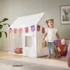 A young girl stands next to a white play tent, holding a pillow and a small suitcase. Náhled obrázku produktu