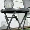A close-up view of a folding side table with a decorative lantern and a folded newspaper on top. Produktbild-Vorschau