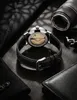 A watch with a black strap is shown on a dark, textured surface, with other accessories like cufflinks and a wallet nearby. Voir les images du produit