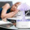 A person sleeping in the background while a humidifier is operating on a desk with a notebook and pen. Voir les images du produit