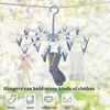 A clothes drying rack with clips is shown hanging from a clothesline, with a teddy bear, socks, and a towel attached. The background is blurred foliage. Produktbild-Vorschau