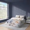 A bedroom with a bed dressed in floral bedding, a large window with natural light casting shadows on the wall. Podgląd zdjęcia produktu