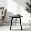 A black round side table with books and a cup on it, next to a chair and a plant. Náhľad obrázku produktu