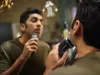 A man is shaving his face in front of a mirror, holding an electric shaver. Produktbild-Vorschau