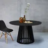A black round dining table with a unique base, paired with a black chair, set against a concrete wall. Produktbild-Vorschau