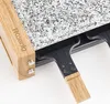 Close-up view of a raclette grill with a granite stone cooking surface and wooden handles. Produktbild-Vorschau