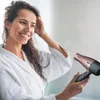 A woman in a white robe is drying her hair with a rose gold and black hairdryer. Produktbild-Vorschau