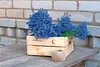 Lavender flowers in a wooden crate on a wooden surface with a brick wall in the background. Produktbild-Vorschau