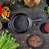A cast iron skillet with various ingredients arranged around it on a dark wooden surface. Produktbild-Vorschau