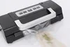 A close-up shot of a black and silver vacuum sealer machine with a silver handle, sealing a clear plastic bag containing a piece of fish and some herbs. Podgląd zdjęcia produktu