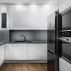 A modern, minimalist kitchen with white cabinets, a dark sink, and stainless steel appliances. Produktbild-Vorschau