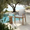 A chair and side table are placed next to a swimming pool under a large tree, with a beach and ocean in the background. Voir les images du produit