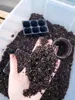 A hand holding soil over a container of soil, with seedling trays and pots in the background. Produktbild-Vorschau