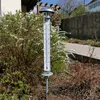 A thermometer in a garden setting with blooming bushes. Náhľad obrázku produktu