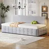 A light gray upholstered daybed with a tufted base and a tall headboard is shown in a well-lit room with a patterned rug on the floor. Produktbild-Vorschau