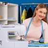 A woman is sewing with a sewing machine in a bright room with shelves and clothes hanging in the background. Produktbild-Vorschau