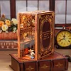 A miniature book nook diorama designed to look like a vintage book, placed on top of other books. The diorama depicts a cozy interior scene with furniture and decor, and has a clear plastic cover. A clock and flowers are visible in the background. Voir les images du produit