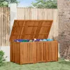 A wooden garden storage box with its lid open, filled with garden tools and hoses, placed on a grassy lawn next to a wooden fence and a brick wall. Podgląd zdjęcia produktu