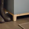 A close-up view of the bottom of a gray shoe cabinet with wooden legs, and a pair of brown boots next to it. Náhled obrázku produktu