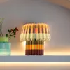 A colorful pleated paper lamp sits on a shelf with a vase of flowers next to it. Produktbild-Vorschau