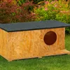 An outdoor cat house made of OSB wood with a black asphalt roof, placed on green grass with bushes and flowers in the background. Náhled obrázku produktu
