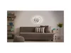A living room with a sofa, ottoman, and a wall-mounted light fixture. Produktbild-Vorschau