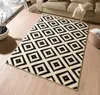 A black and cream diamond patterned rug is laid out on a light wood floor in a living room setting. Podgląd zdjęcia produktu