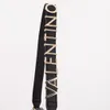 A close-up of a black handbag strap with gold Valentino logo letters. Voir les images du produit