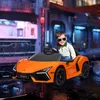 A young boy wearing sunglasses is sitting in an orange electric toy car, with a blurred urban night scene in the background. Produktbild-Vorschau