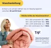 A woman is holding a folded duvet, with text providing washing instructions and washing machine size recommendations. Produktbild-Vorschau