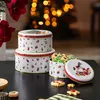 Christmas-themed cookie tins and cookies are arranged on a dark surface, with a blurred Christmas tree in the background. Produktbild-Vorschau
