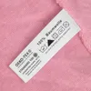 A close-up of a clothing care label attached to a pink fabric. Produktbild-Vorschau