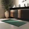 A dark green rug is placed on a light gray floor in a room with a wooden cabinet and a large potted plant. Produktbild-Vorschau