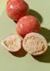 Three raspberry crispy balls with white chocolate coating, two of which are whole and one is cut in half, are shown on a light green surface. Produktbild-Vorschau