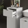 A close-up view of a white bathroom cabinet with one drawer partially open, revealing its interior and drawer slides. Decorative reeds in a diffuser and a bottle of liquid are on top of the cabinet. Náhled obrázku produktu