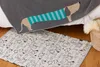 A close-up view of a grey blanket with a dachshund pattern and a small rug with a repeating dachshund pattern, placed on a wooden floor next to a bed. Produktbild-Vorschau