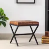A brown leather upholstered stool with a black metal X-frame base is shown in a room setting. Náhľad obrázku produktu