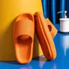 Paar leuchtend orangefarbene klobige Slide-Sandalen mit strukturierten Riemen und Sohlen, an gelber Fläche lehnend Náhľad obrázku produktu