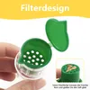 A hand holding a green and clear manual citrus juicer with a lid open. A small inset image shows seeds inside the juicer's filter. Produktbild-Vorschau