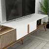 A modern TV stand with a white top and wood accents, featuring slatted doors and angled legs, placed in a living room setting. Náhled obrázku produktu