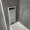 A shower screen is installed over a bathtub in a bathroom with concrete-look walls. Produktbild-Vorschau