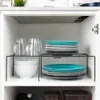 A kitchen cabinet interior showing a shelf organizer holding plates and bowls, with mugs on top. Podgląd zdjęcia produktu