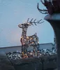 A decorative reindeer with LED lights sits on a stone border in front of a white wall. Podgląd zdjęcia produktu