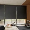 A woman is doing exercises on a mat in front of large windows with blinds. Voir les images du produit