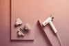 A white Shark SpeedStyle hair dryer with multiple attachments is arranged on pink platforms against a pink and orange gradient background. Voir les images du produit