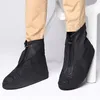 A person wearing black shoe covers over their shoes and tan pants. Produktbild-Vorschau