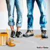 Two people's legs are shown, wearing paint-splattered jeans and work boots, standing next to a can of yellow paint and a paintbrush. Náhľad obrázku produktu